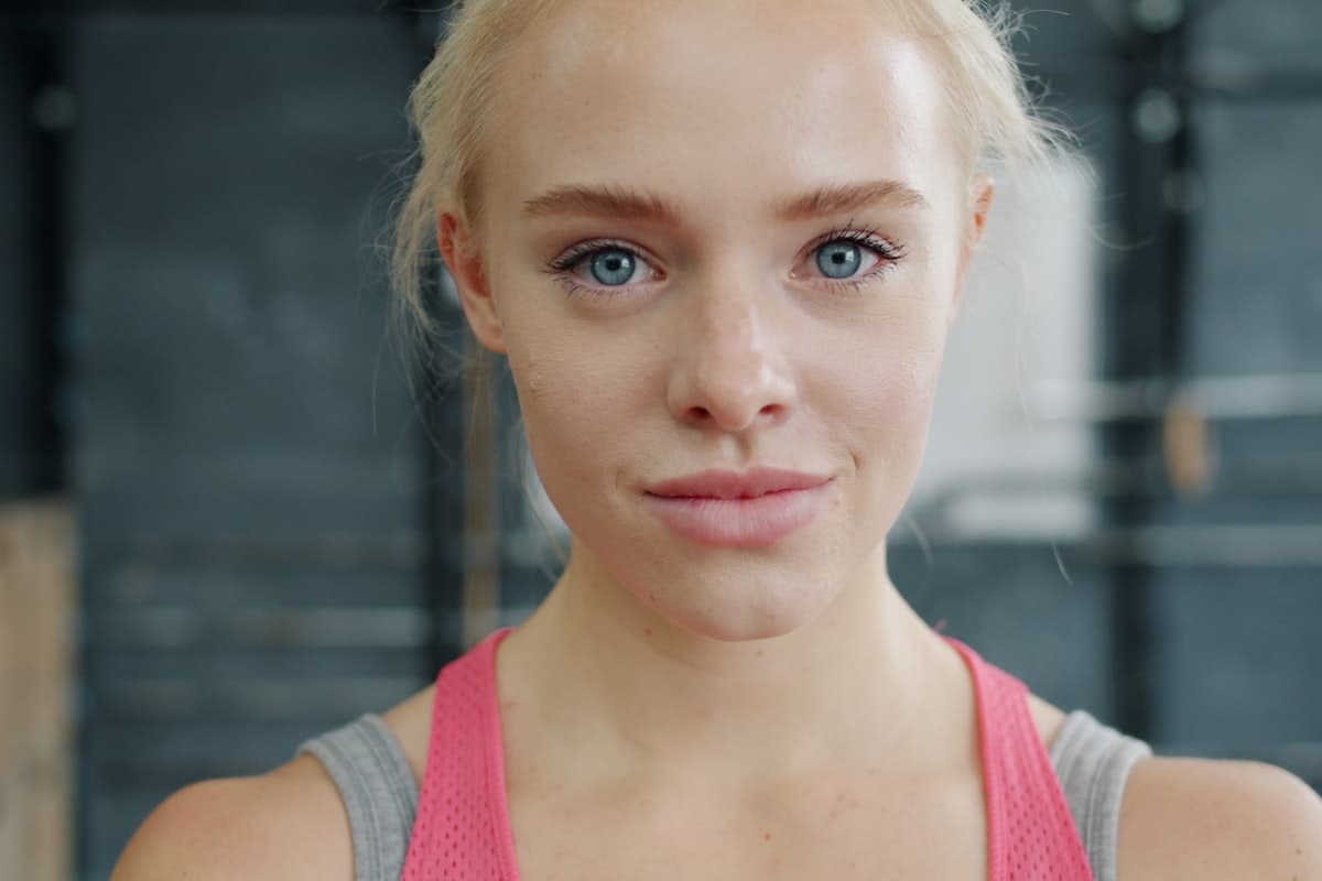 A woman reviewing her workout journal between sets at the gym, with a barbell and weight plates visible in the background.