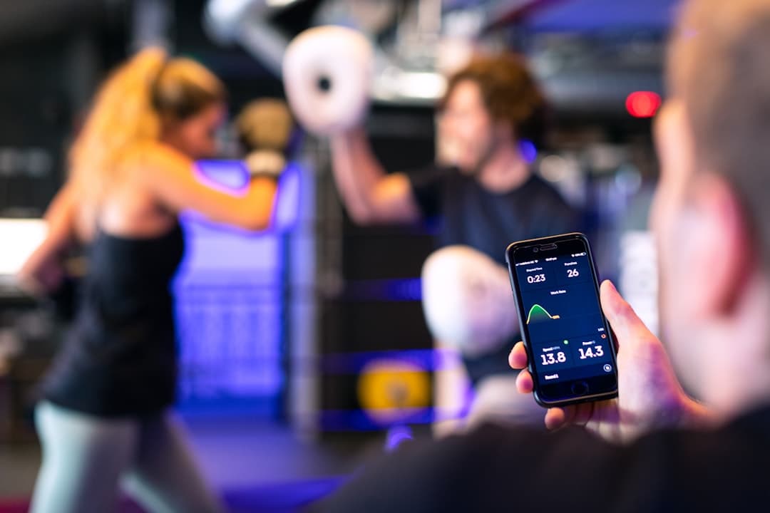 An Android phone displaying the FitNotes workout app next to an open paper logbook with handwritten training data on a gym bench