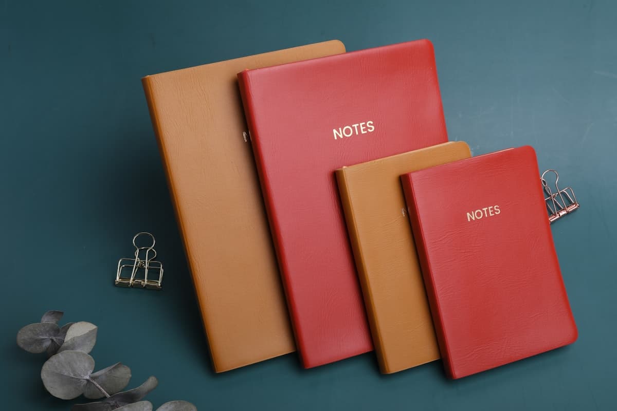 Several different training logbooks spread out on a gym bench next to a barbell and chalk